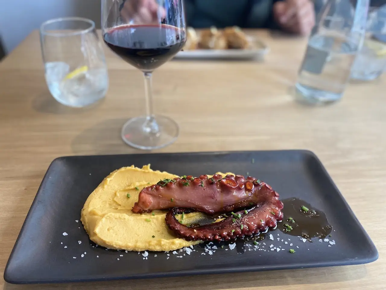 Grilled octopus tentacle over a yellow purée on a dark slate plate