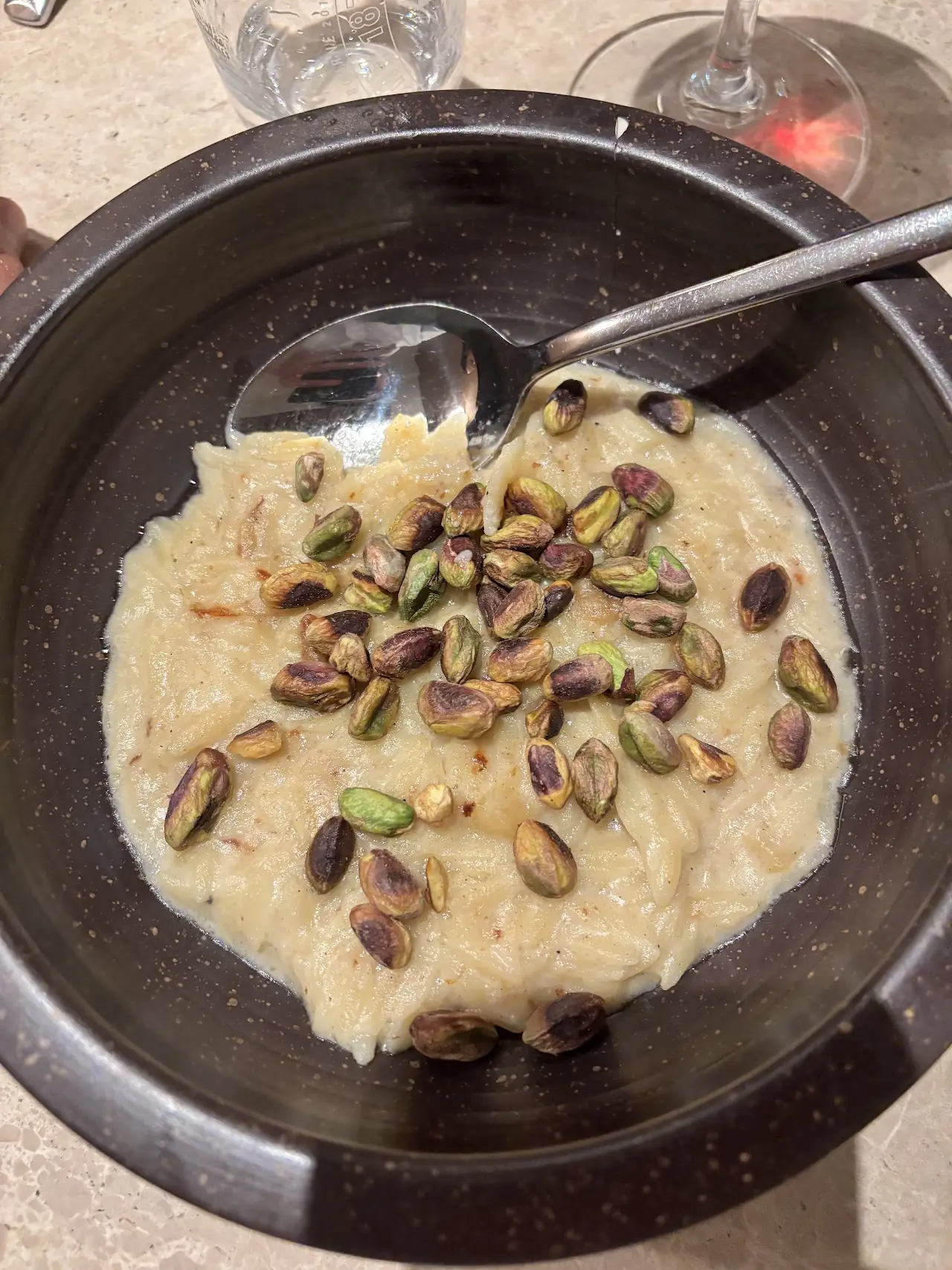 Creamy rice topped with pistachios in a dark bowl
