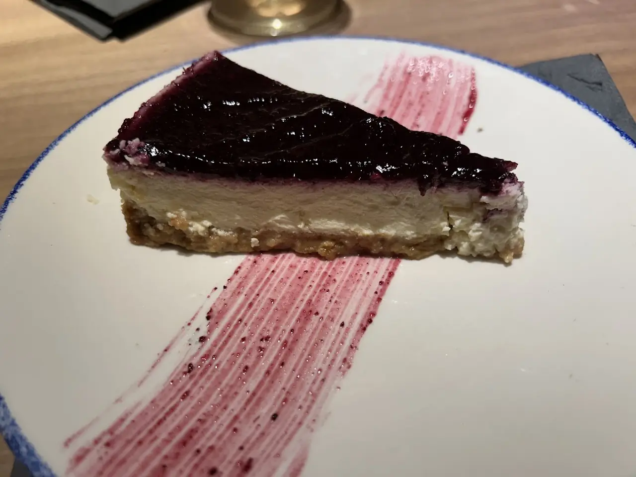 A slice of cheesecake with a dark berry topping and a swipe of berry sauce
