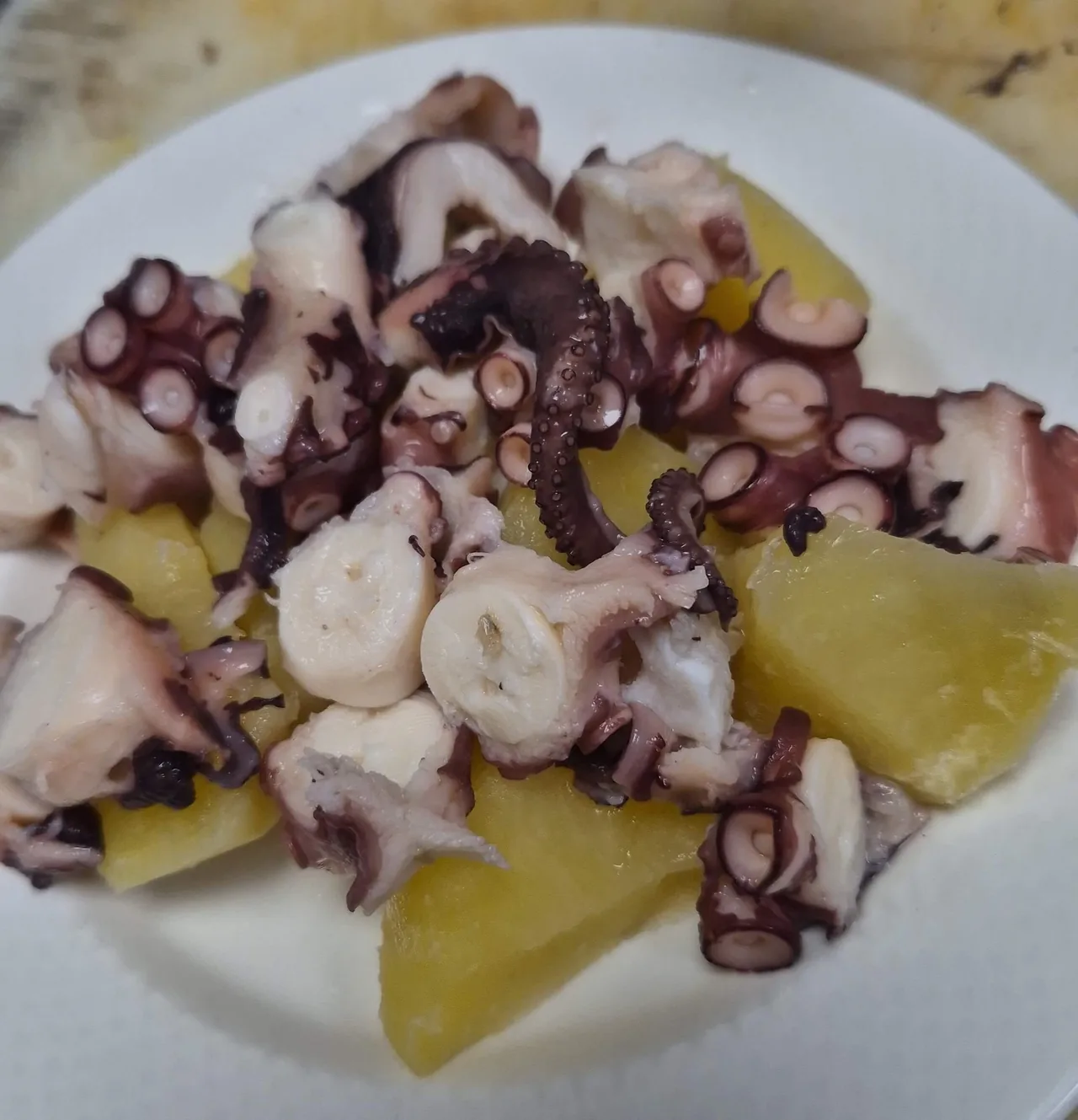 Chunks of boiled octopus with potato wedges on a white plate