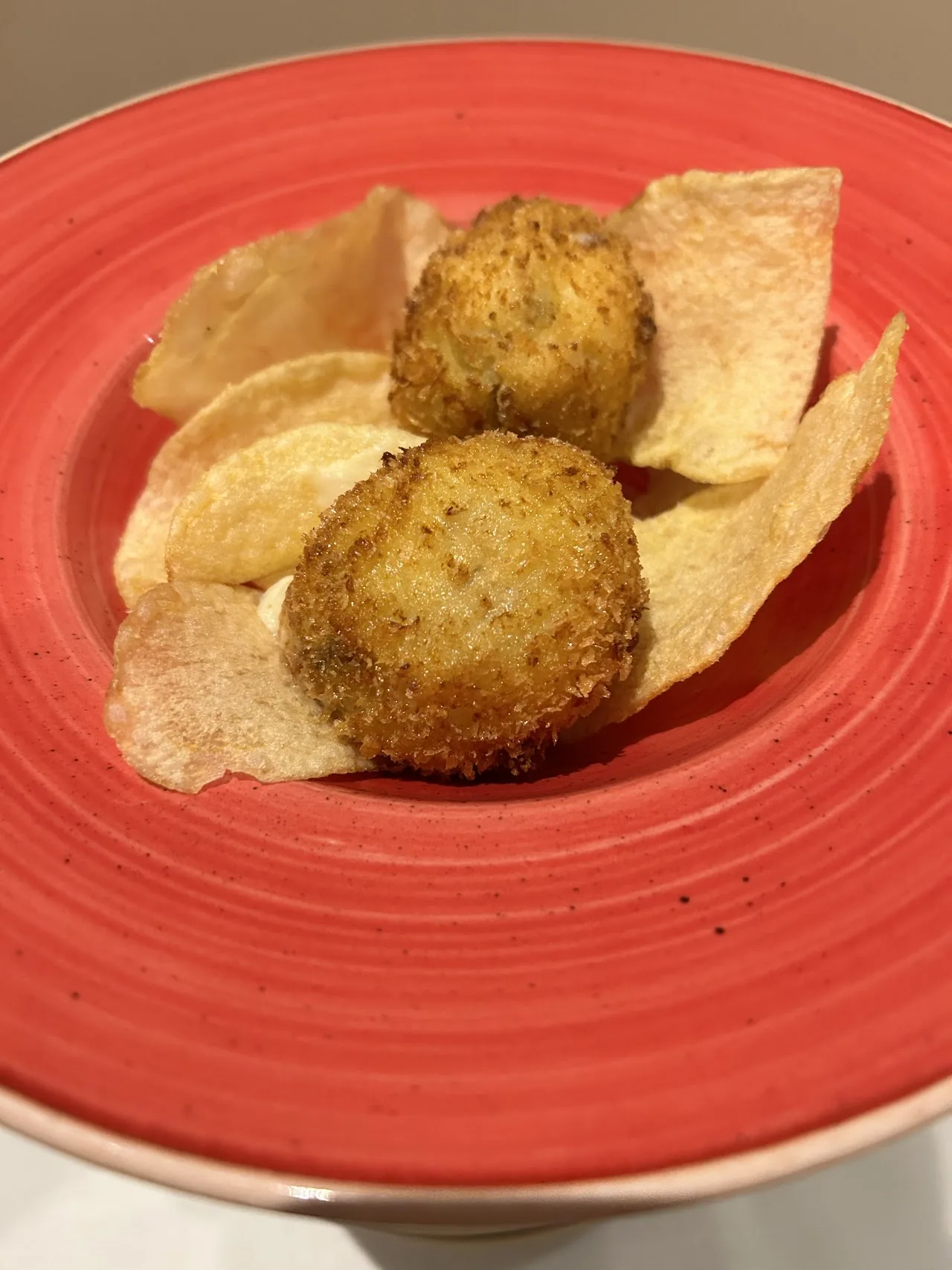 Two breaded croquettes with potato chips on a red plate