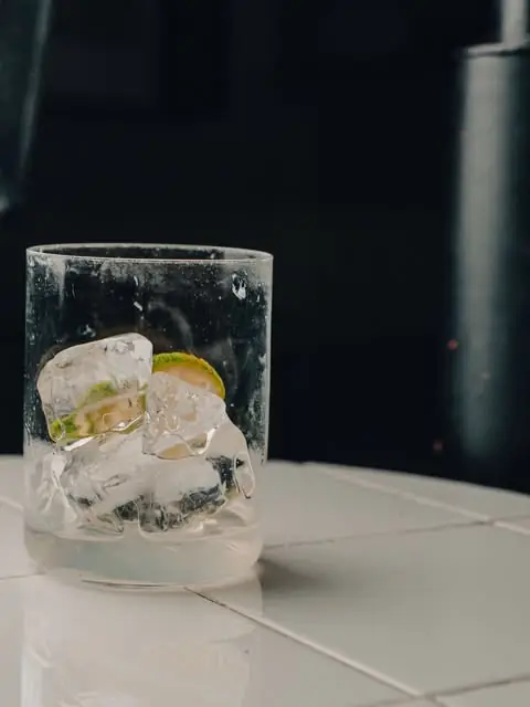 Cocktail glass with ice and a lime wedge on a white tiled table