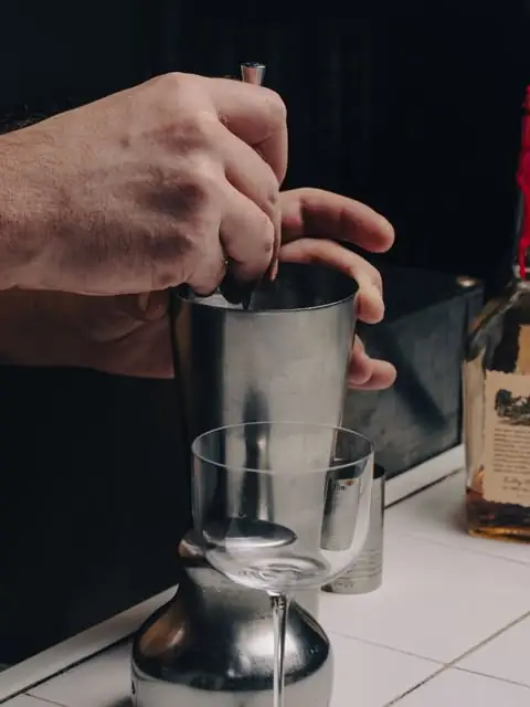 Bartenders hands mixing a cocktail with a metal shaker tin over an empty glass