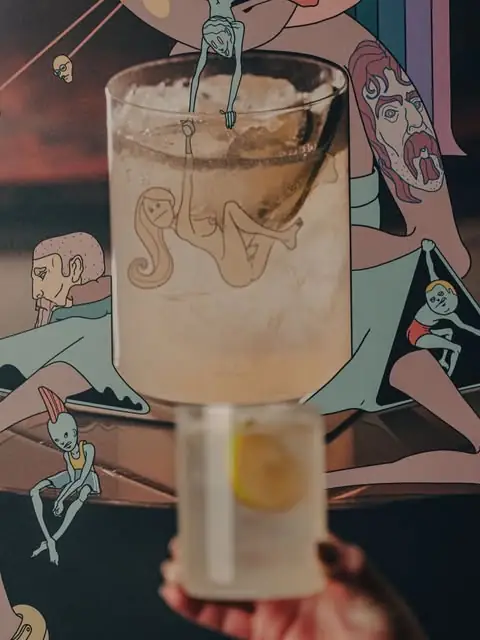 Cocktail in a glass with ice, held up against a colourful mural backdrop
