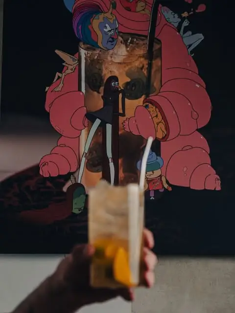 Cocktail with an orange garnish and straw held up against a colourful mural backdrop