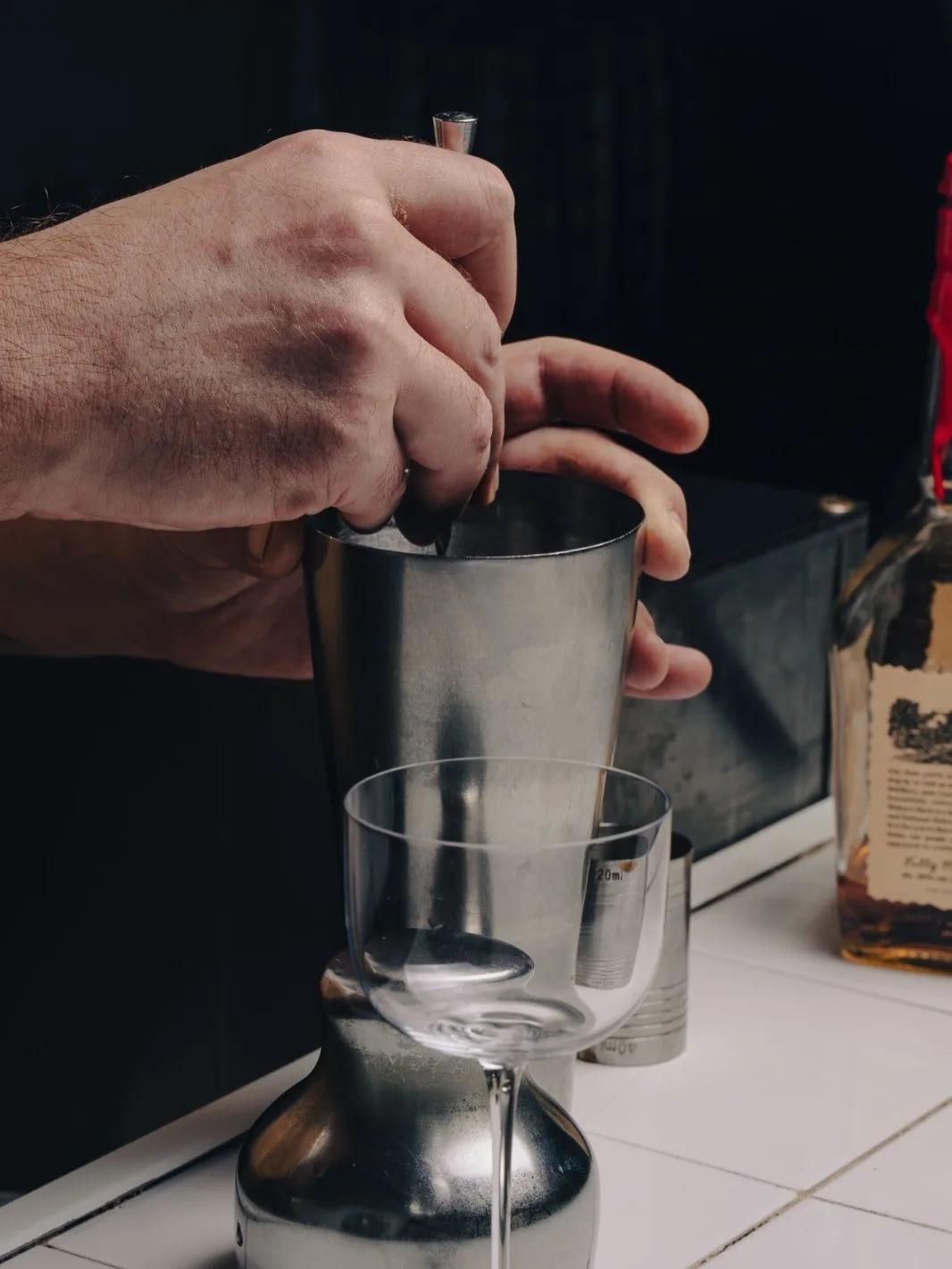 A hand stirring a drink in a metal shaker on a bar counter