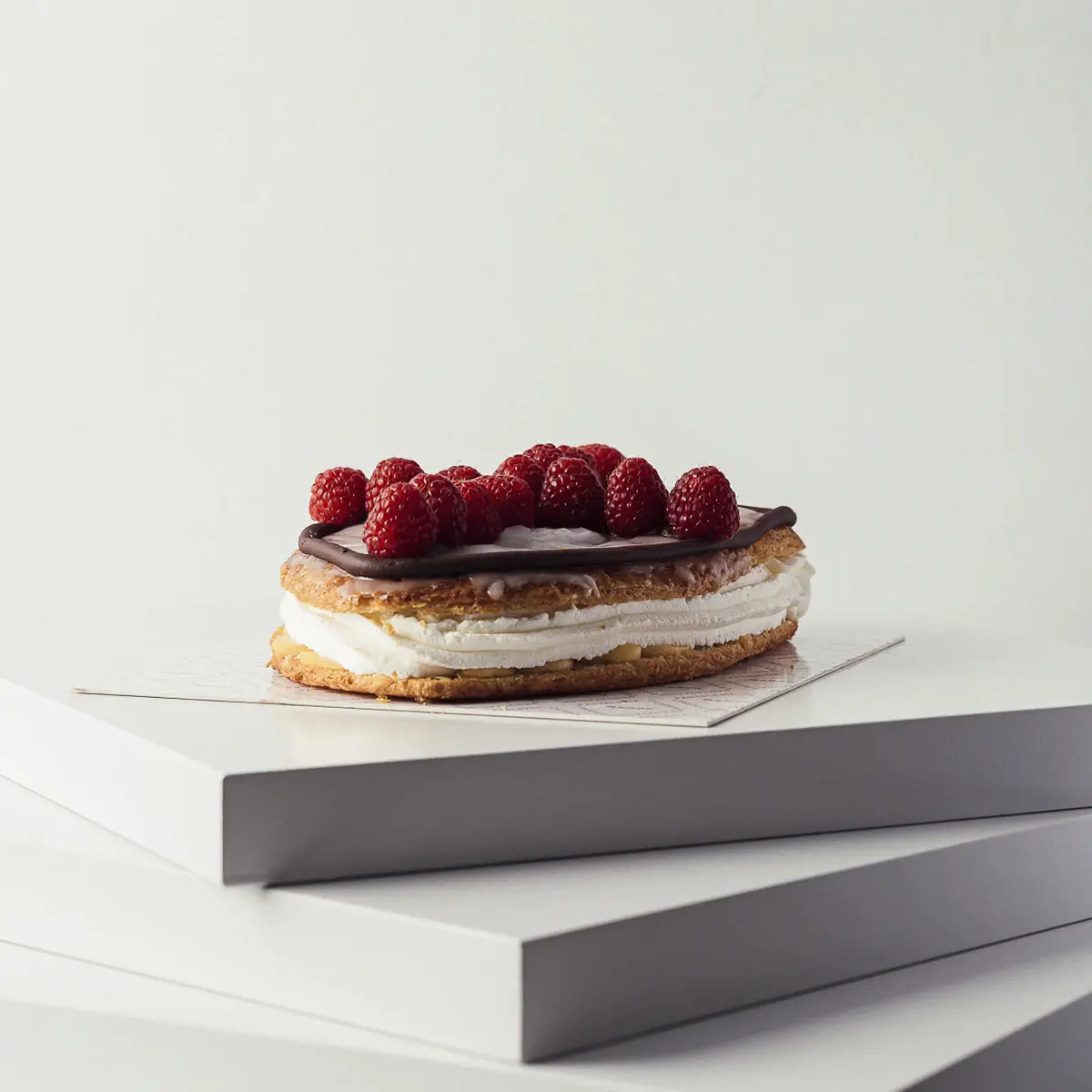 A layered mille-feuille pastry topped with fresh raspberries on a plain white surface at Semon