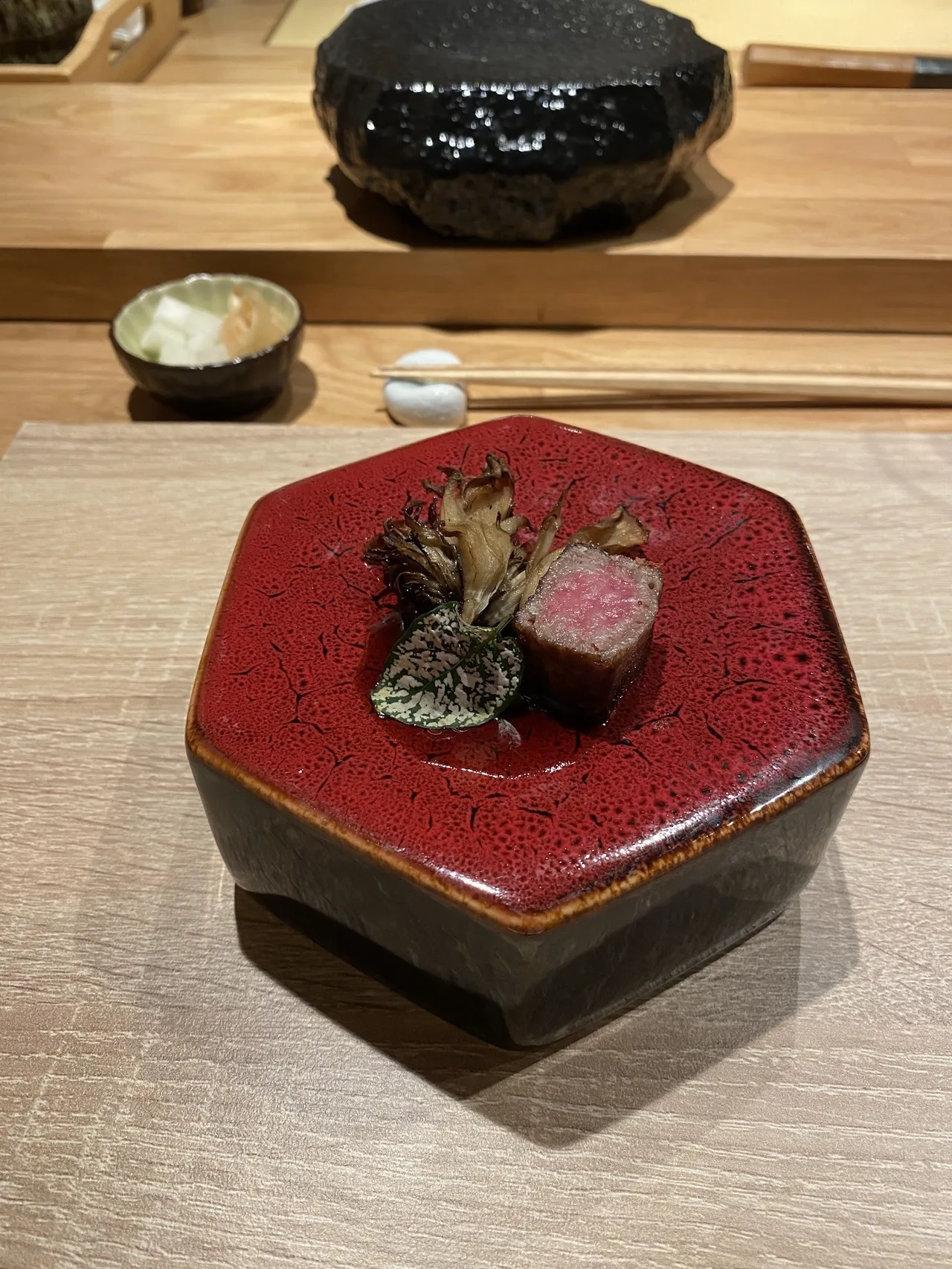 A seared cube of meat beside roasted mushrooms on a red hexagonal dish