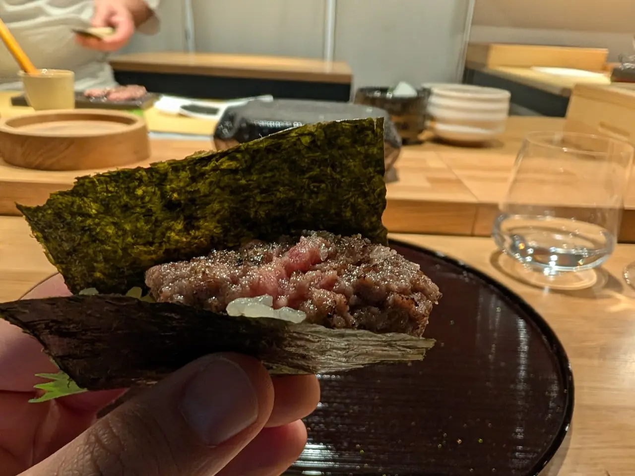 Hand holding a nori-wrapped bite filled with minced meat, held up close to the camera