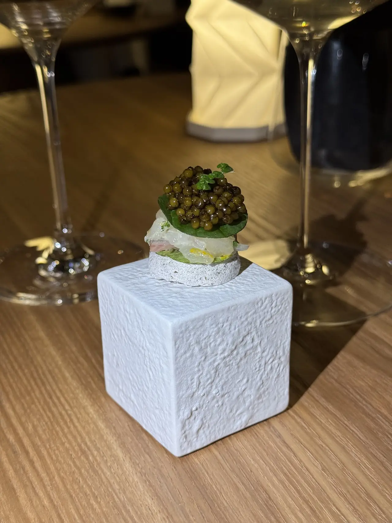 A small bite topped with caviar and herb garnish served on a white cube pedestal