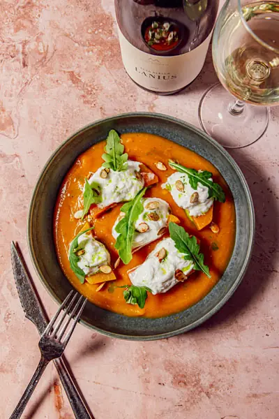 Burrata pieces with arugula and toasted almonds over an orange tomato-based sauce, served in a dark bowl beside a glass of white wine — Sensi Tapas