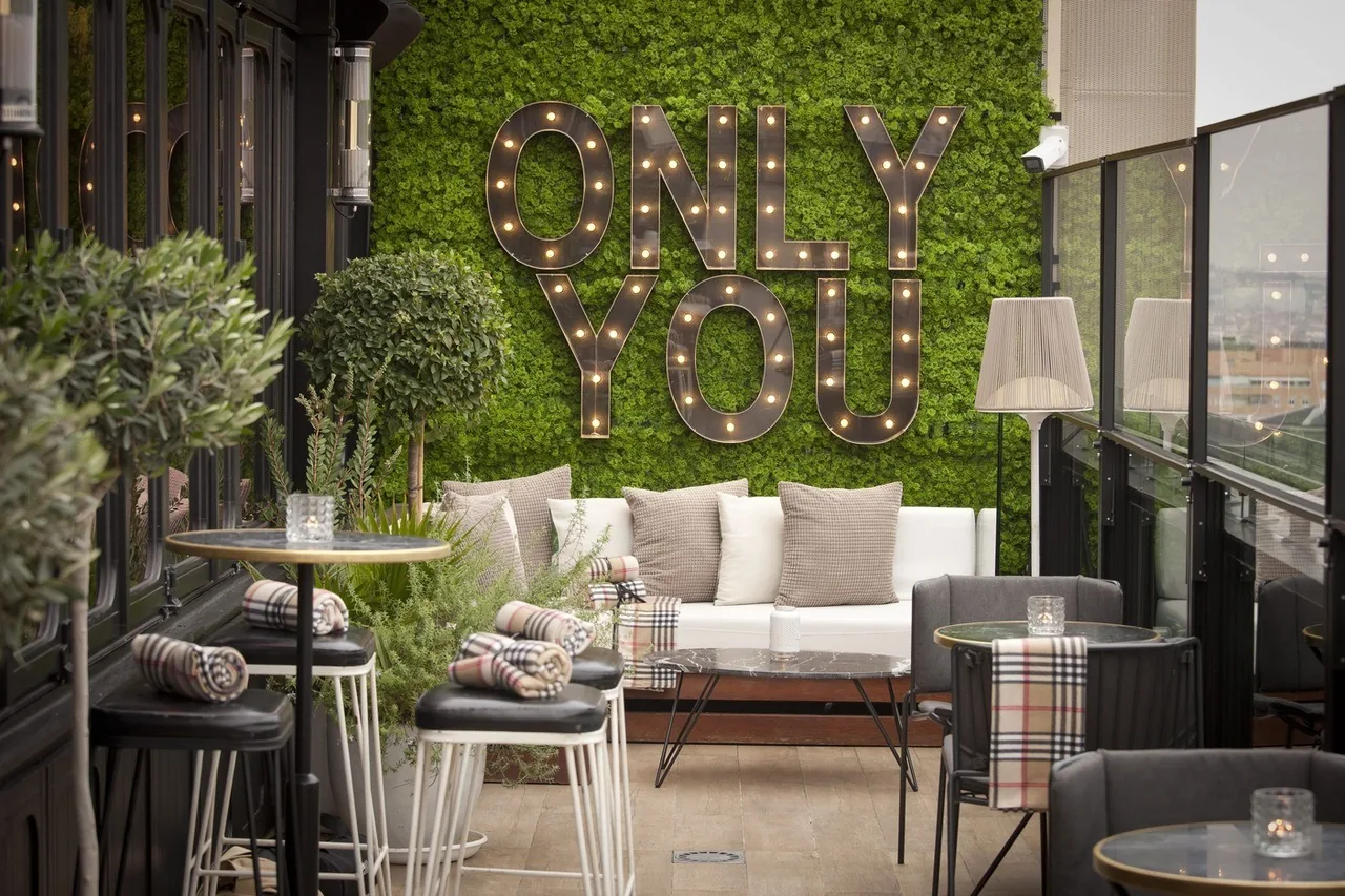 A lounge area with sofas and small tables in front of a green moss wall