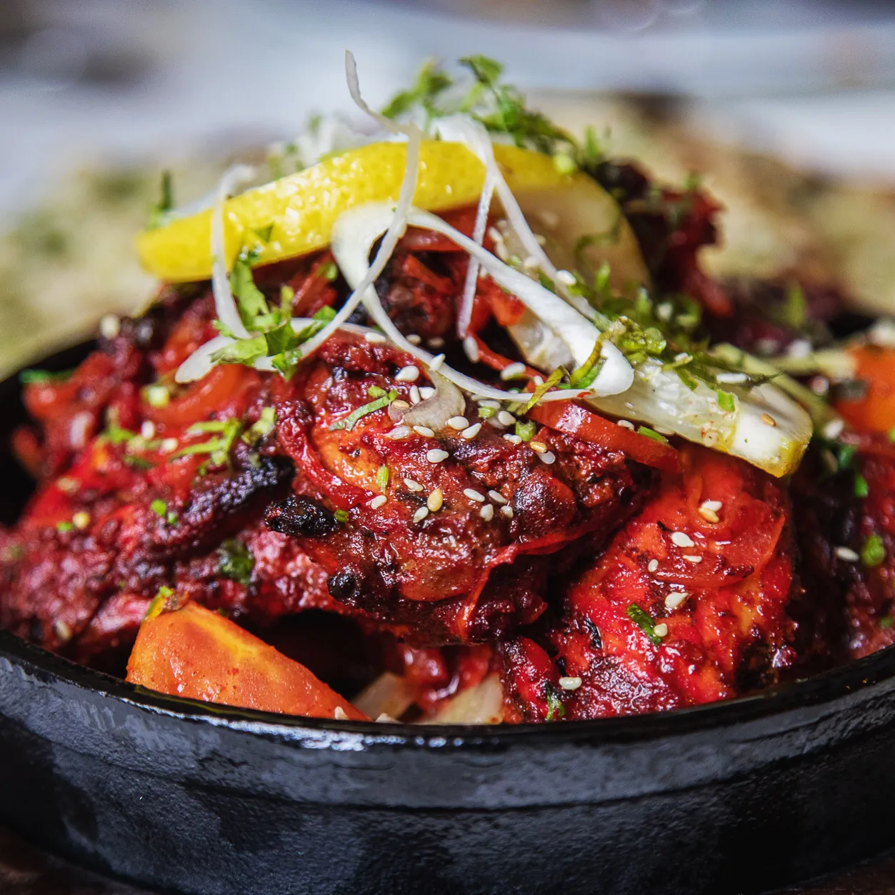 Charred tandoori chicken pieces in a black dish with lemon