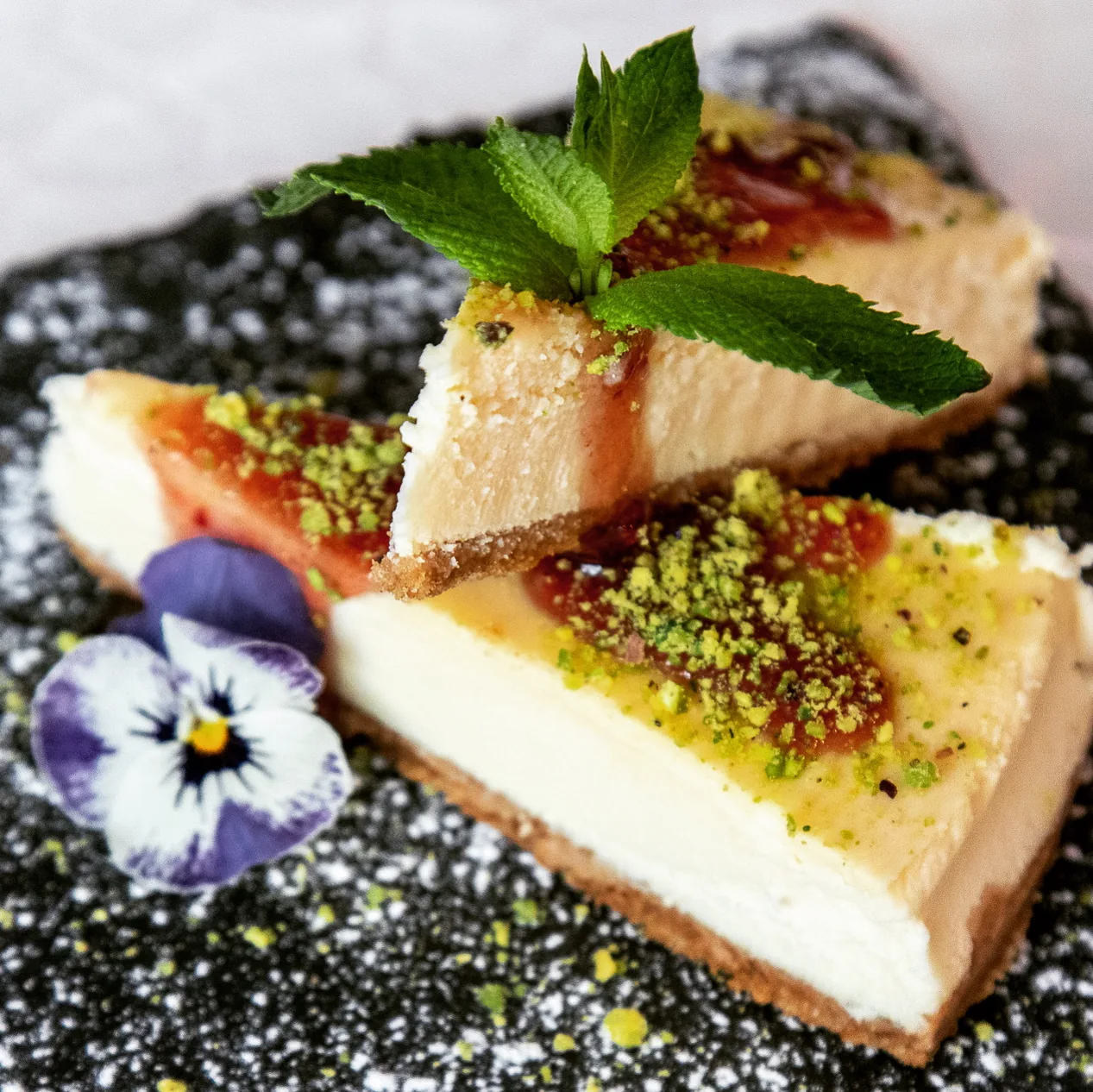 Slices of cheesecake topped with mint and fruit sauce