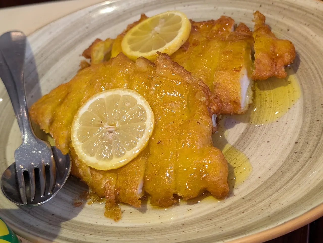 Fried fish fillet topped with lemon slices in a savory sauce