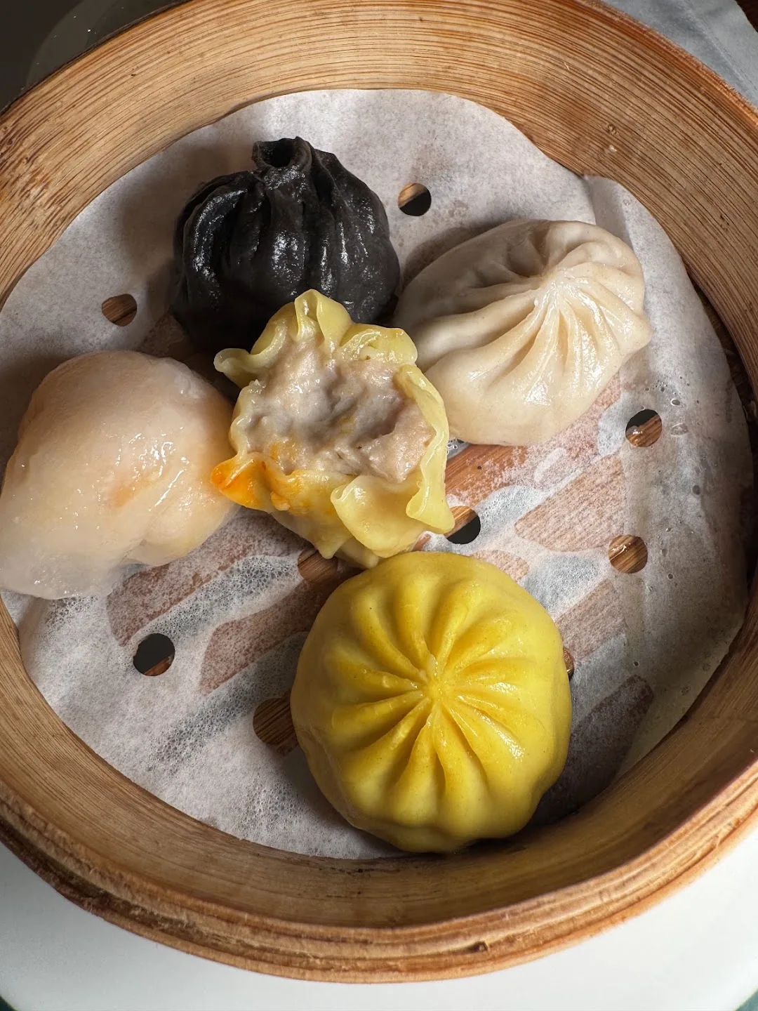Bamboo steamer with five colorful dumplings including a black dumpling and a yellow bao