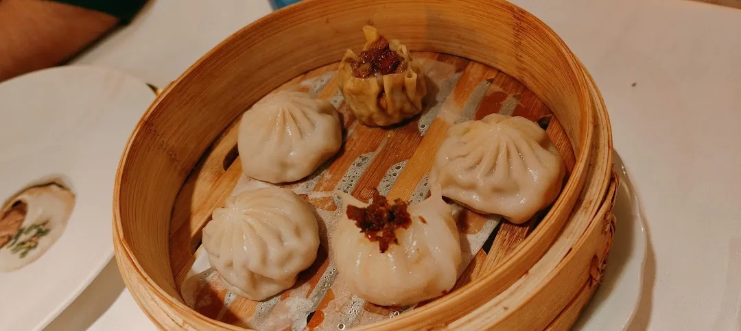 Bamboo steamer with four pork xiaolongbao dumplings and one shumai dumpling topped with crispy garlic