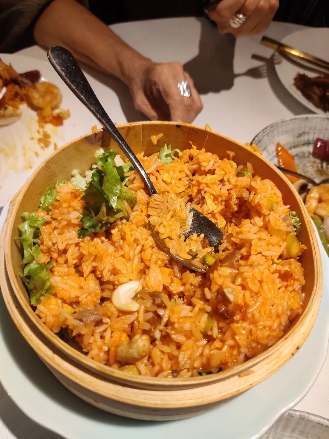 Bowl of orange fried rice with cashews and lettuce garnish, spoon resting inside