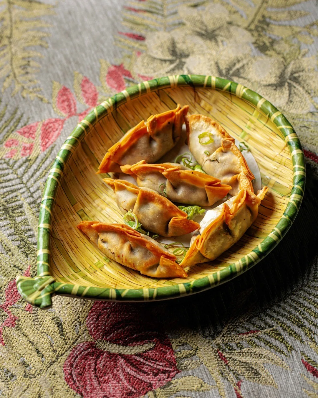 Pan-fried dumplings arranged in a leaf-shaped dish on a patterned surface
