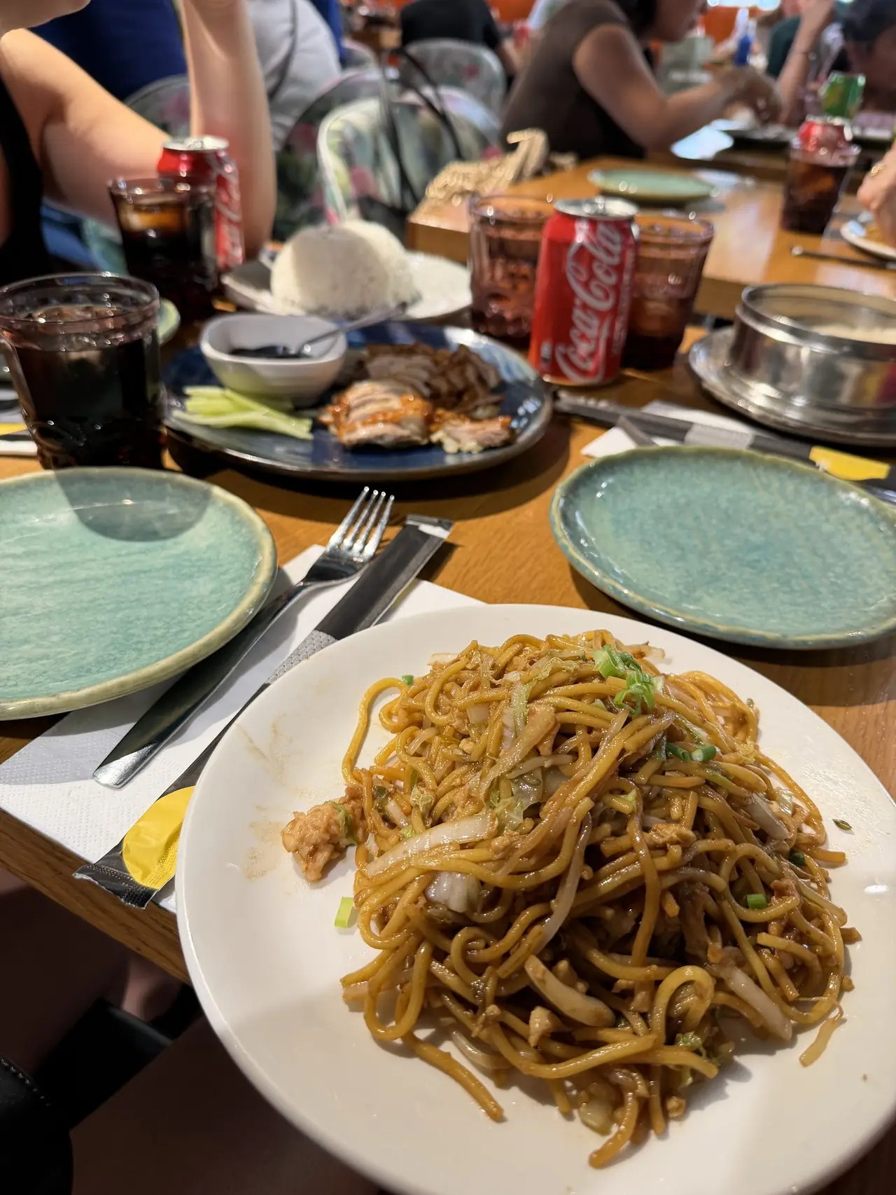 Plate of stir-fried noodles with cabbage and scallions, with roast meat visible on the table behind
