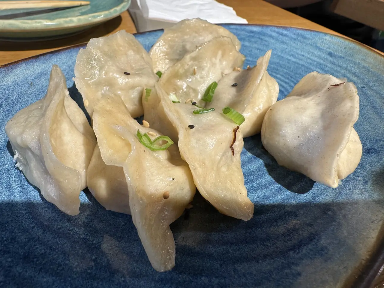 Steamed dumplings topped with scallions and sesame seeds on a blue plate