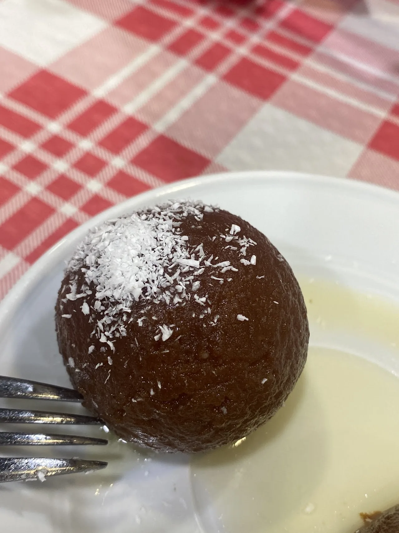 A gulab jamun dessert ball dusted with sugar in cream sauce
