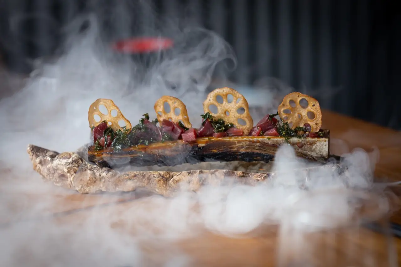 Diced red tuna tartare with fried lotus root crisps and crisp seaweed on a stone slab, wreathed in dry-ice smoke