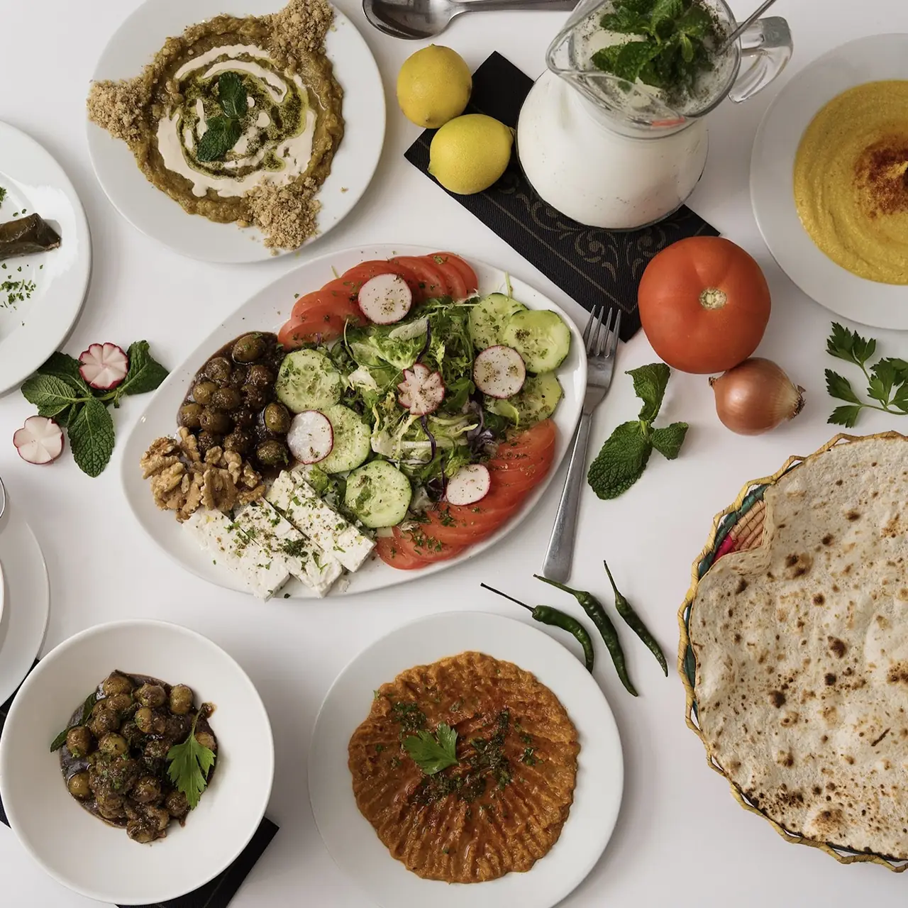 Overhead spread of Persian mezze at Restaurante Shiraz: baba ghanoush, hummus, a fresh salad with feta and walnuts, marinated olives, kashk-e bademjan, and flatbread with lemon and yogurt-mint drink on the side