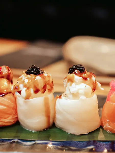 Row of nigiri-style sushi wrapped in white fish and topped with creamy sauce and black caviar