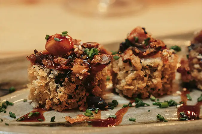 Crispy rice bites topped with glazed sauce, chives and sesame on a ceramic plate