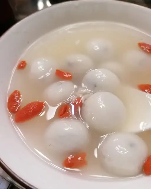 White glutinous rice balls (tang yuan) in a clear broth with goji berries in a white bowl