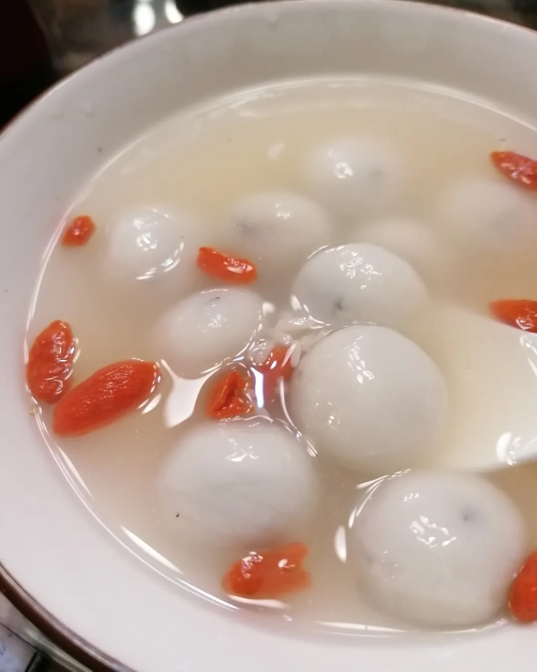 A bowl of soup with white glutinous rice balls and goji berries