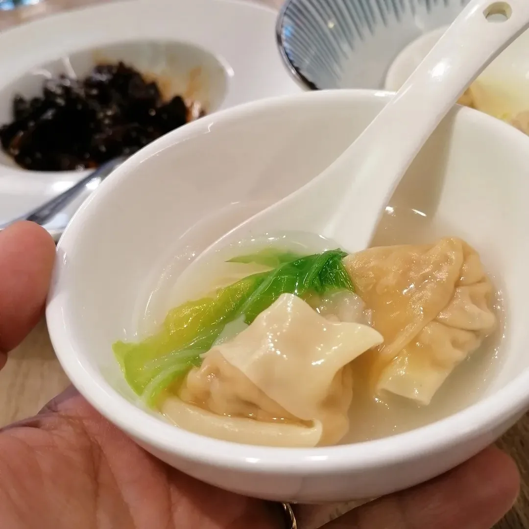 A hand holding a bowl of dumplings in broth