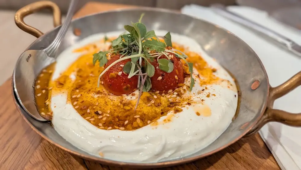 Labneh with roasted tomatoes, herbs, sesame, and chili oil in a copper pan at Silan