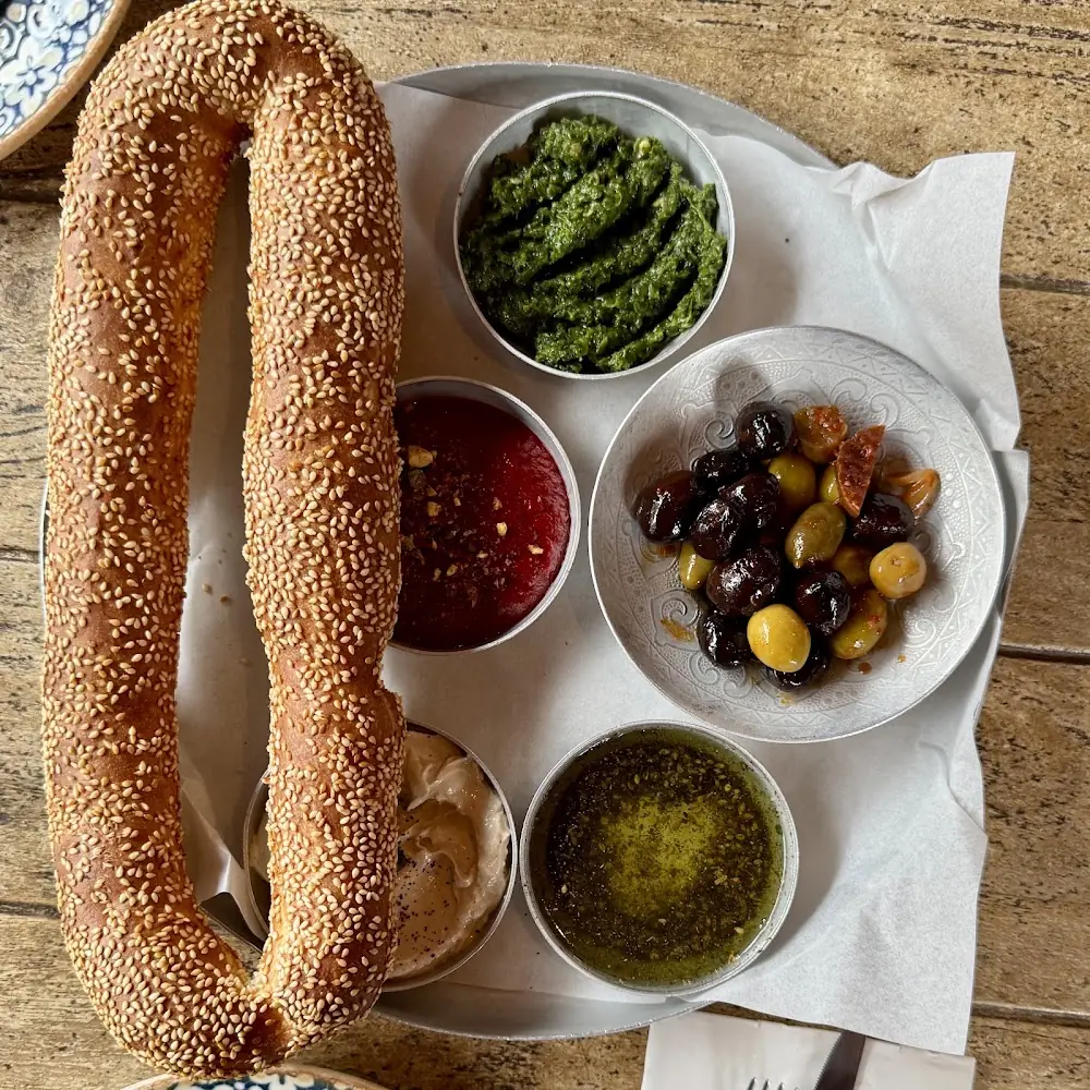 Sesame-crusted bread loaf with bowls of olives, hummus, harissa, and olive oil at Silan