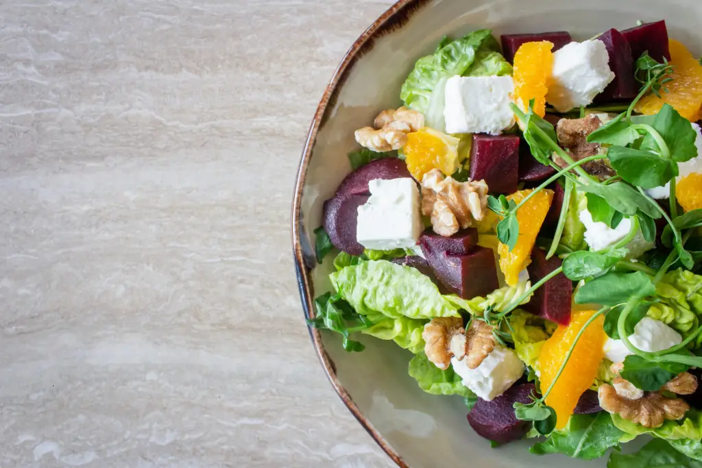 Overhead view of a salad with roasted beetroot, goat cheese cubes, orange segments, walnuts, and pea shoots on a ceramic plate, at Sinfonía