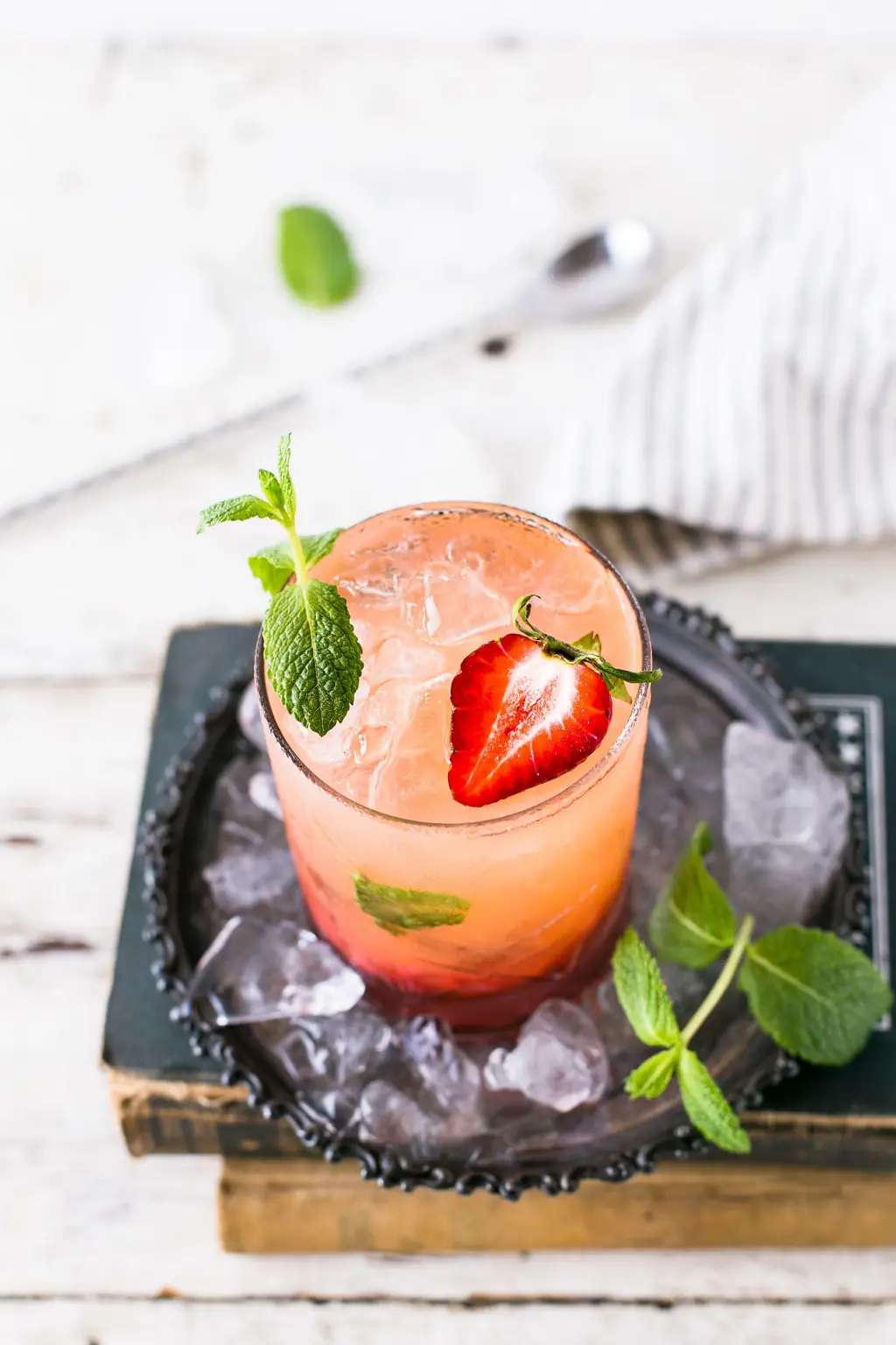 Overhead view of a pink cocktail with ice, a strawberry half, and mint sprigs served in a glass on a dark tray, at Sinfonía