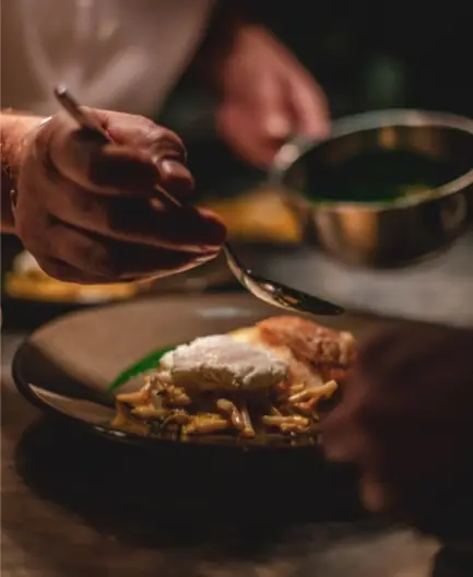 Close-up of a chef's hand spooning a garnish onto a plated dish with rice and mushrooms, at Sinfonía