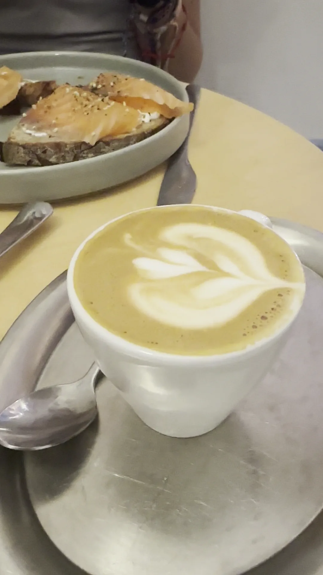 A pastry on a plate next to a latte with heart-shaped foam