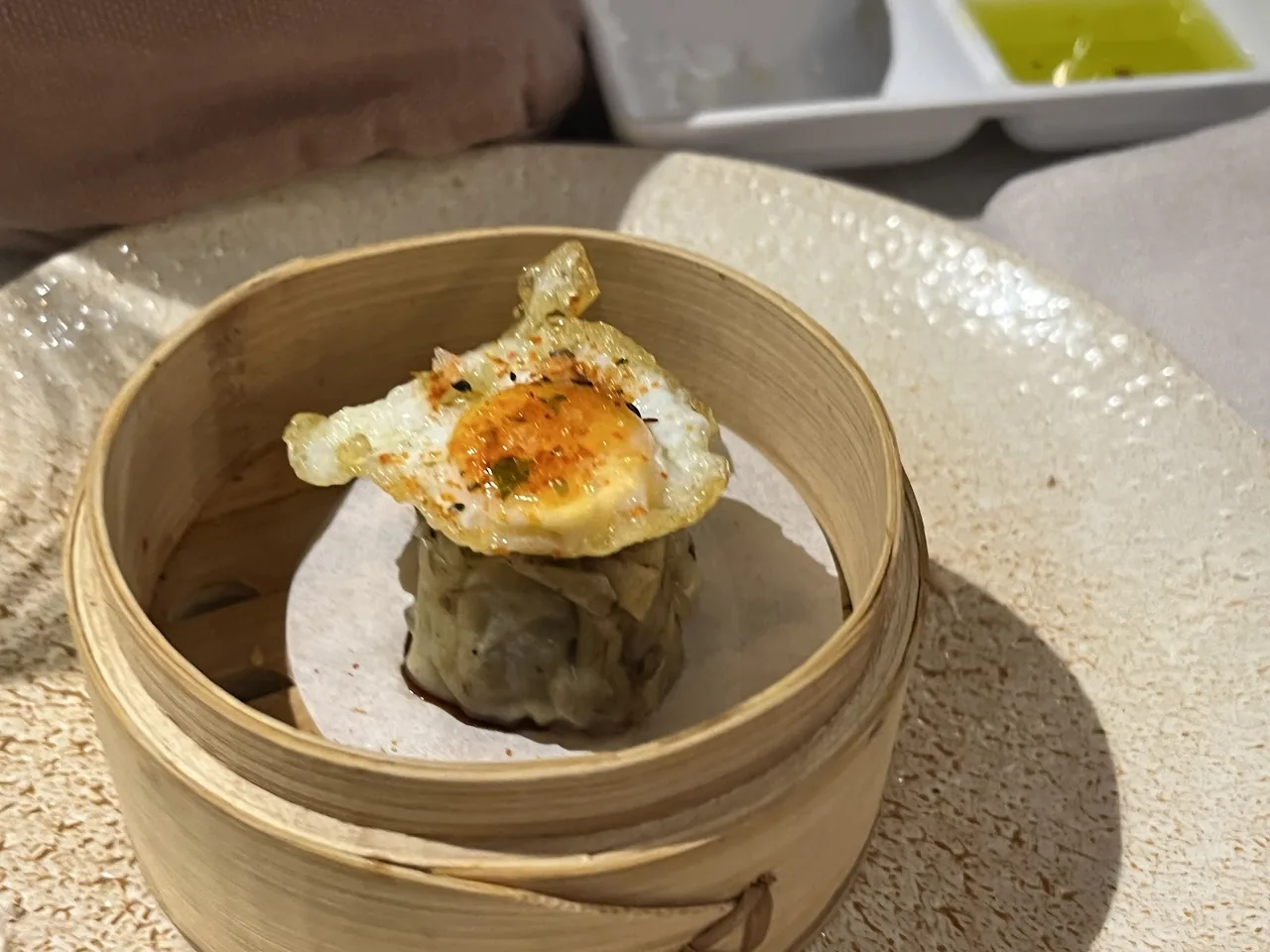 A bamboo steamer holding a dumpling topped with a fried egg