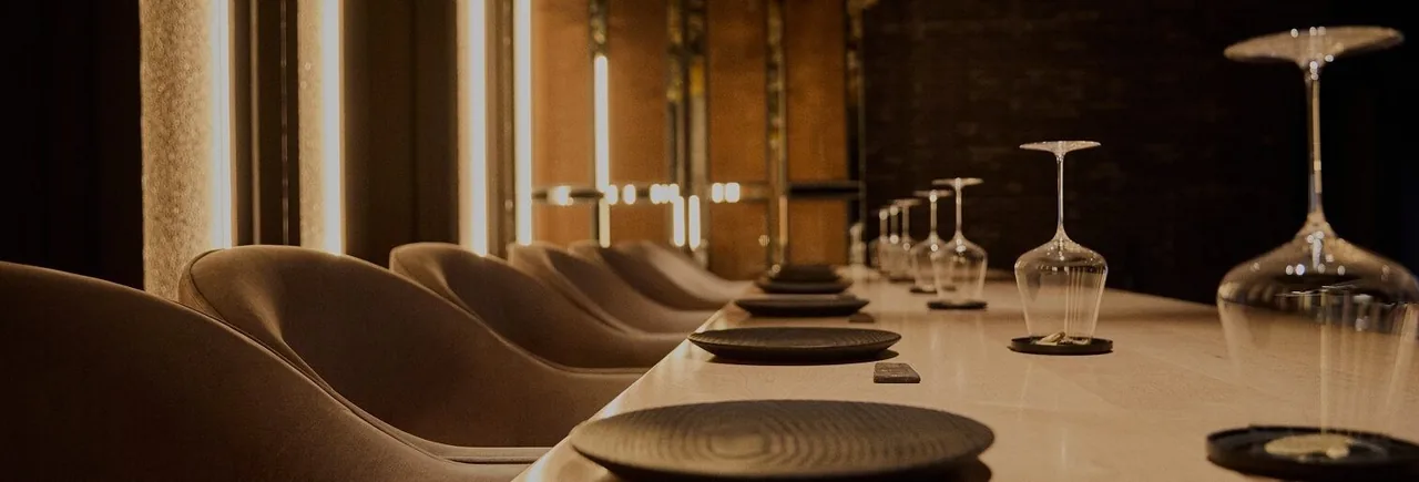 A long counter with cushioned chairs and wine glasses in a warmly lit room