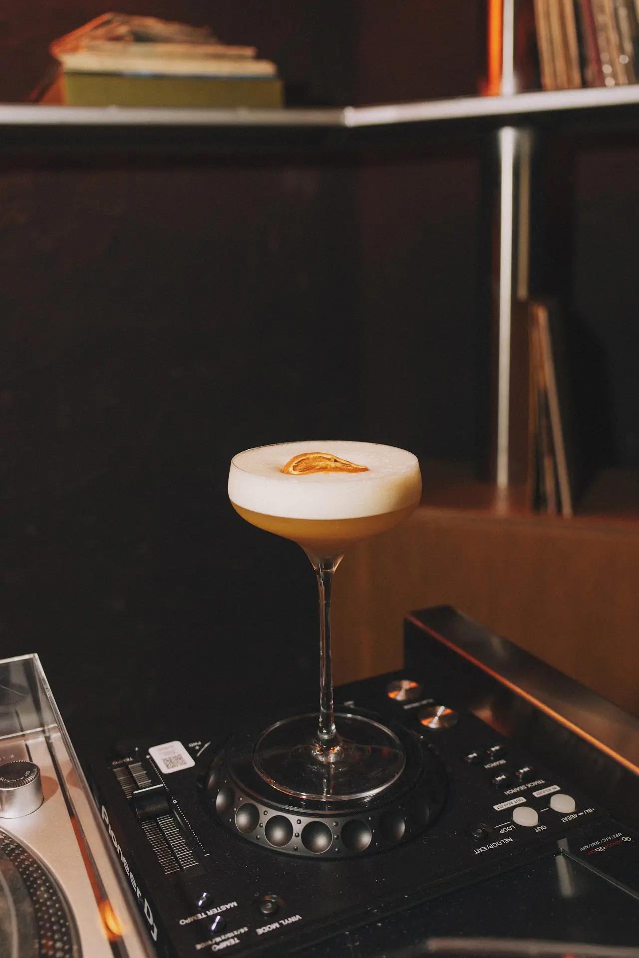A pale cocktail garnished with a citrus twist, set on a DJ turntable
