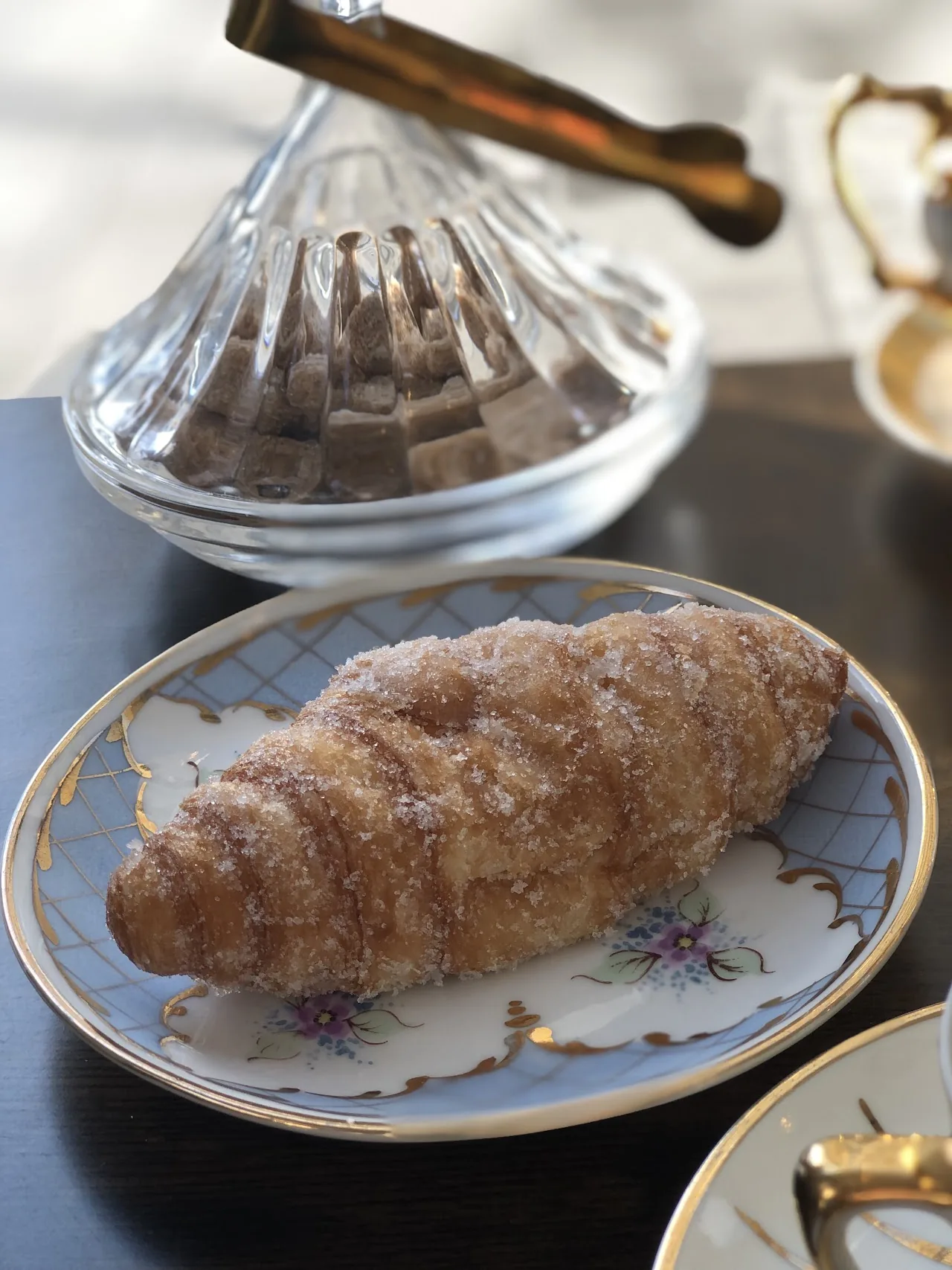 A sugared croissant on a floral plate with a glass dessert cup behind it