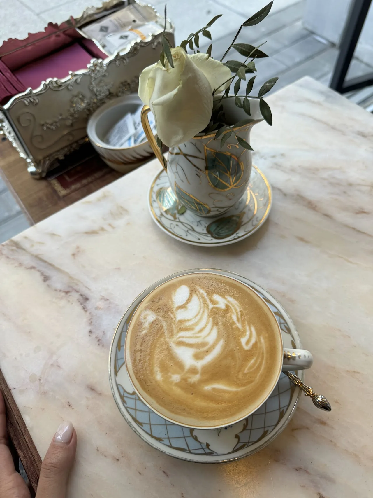 A cappuccino with swan-shaped latte art next to a small flower vase