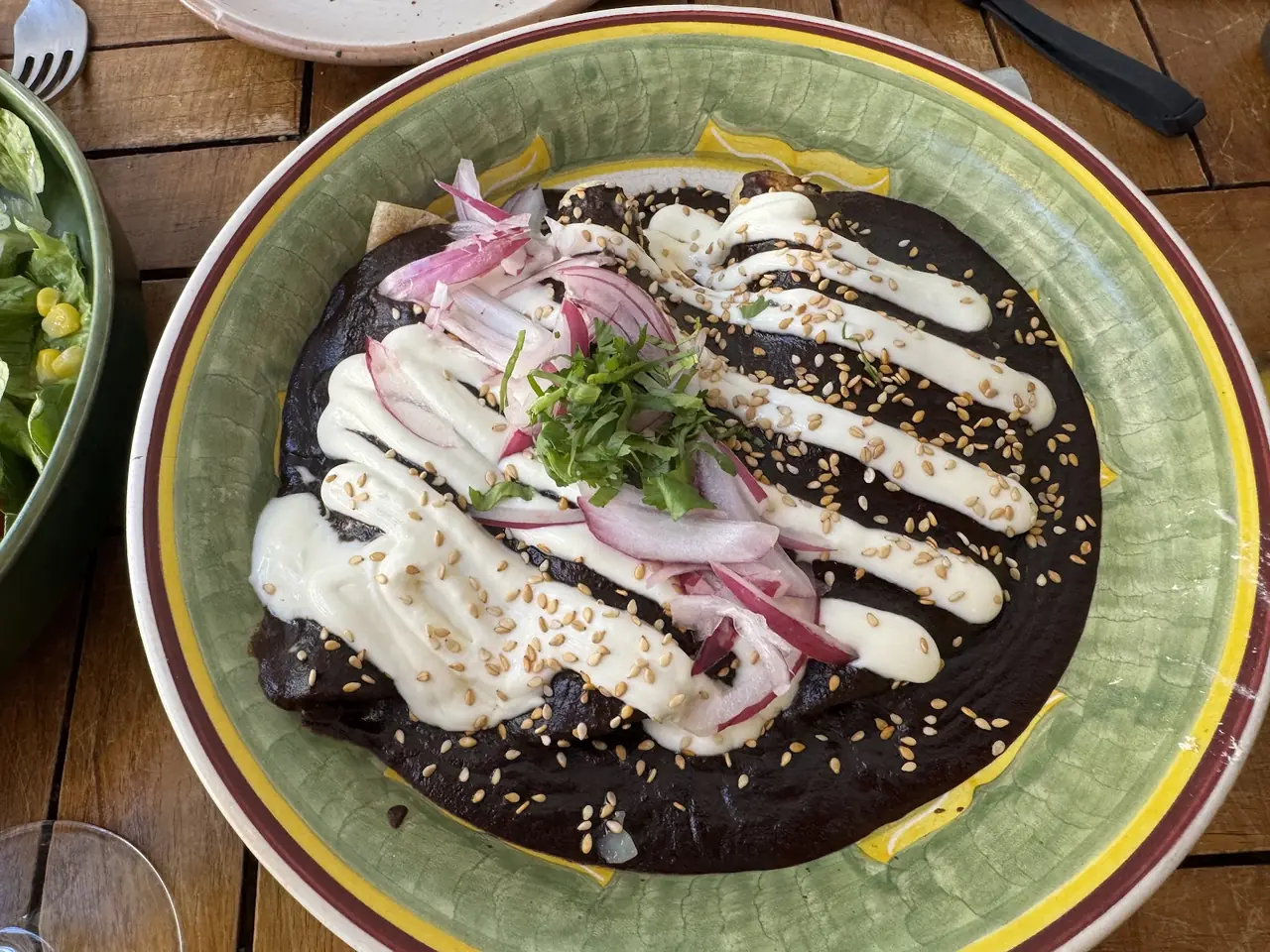 Enchiladas in mole sauce topped with crema, sesame seeds, pickled onion and cilantro