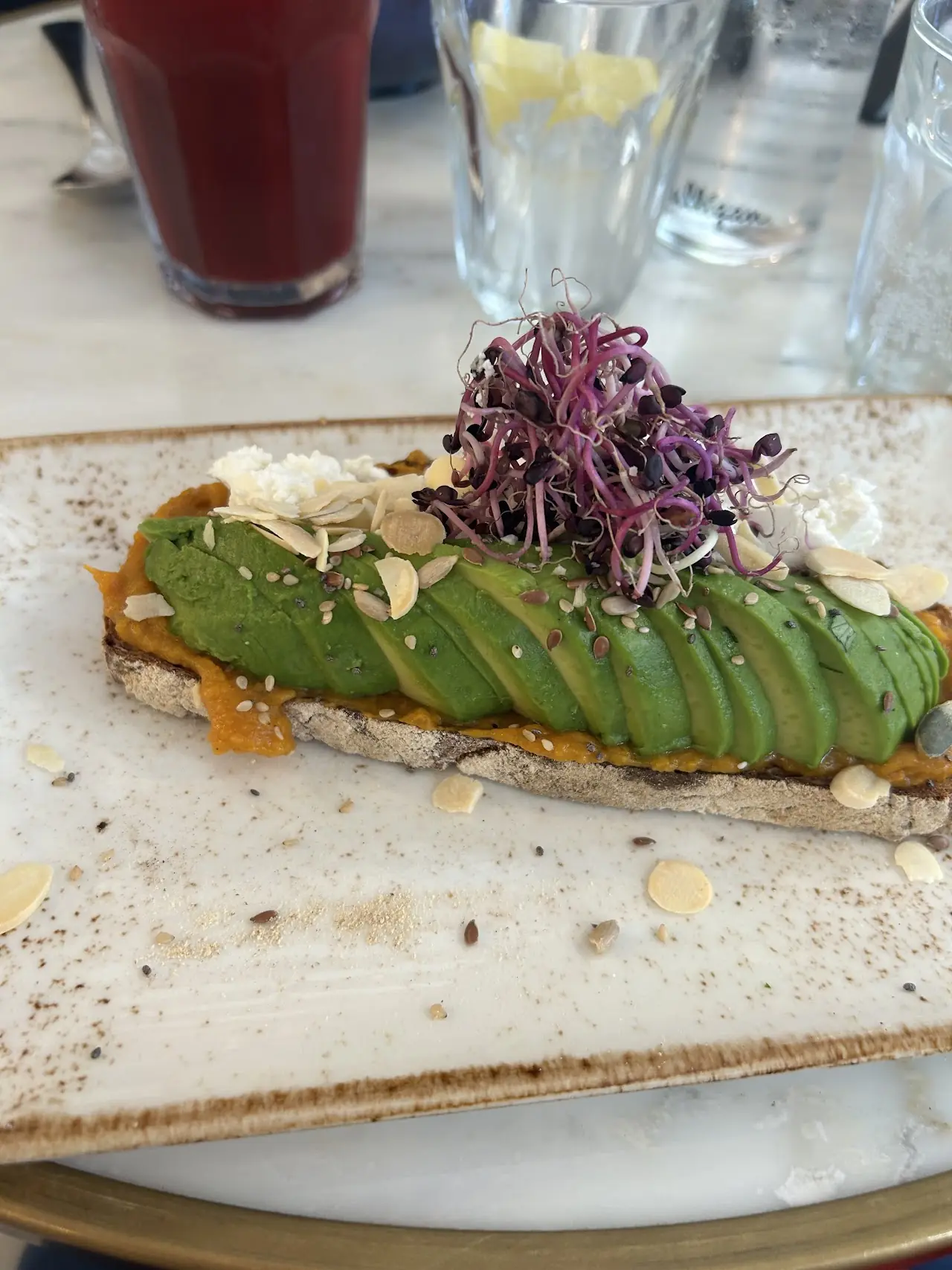 Avocado toast topped with sliced avocado, purple sprouts, and seeds on a wooden board.