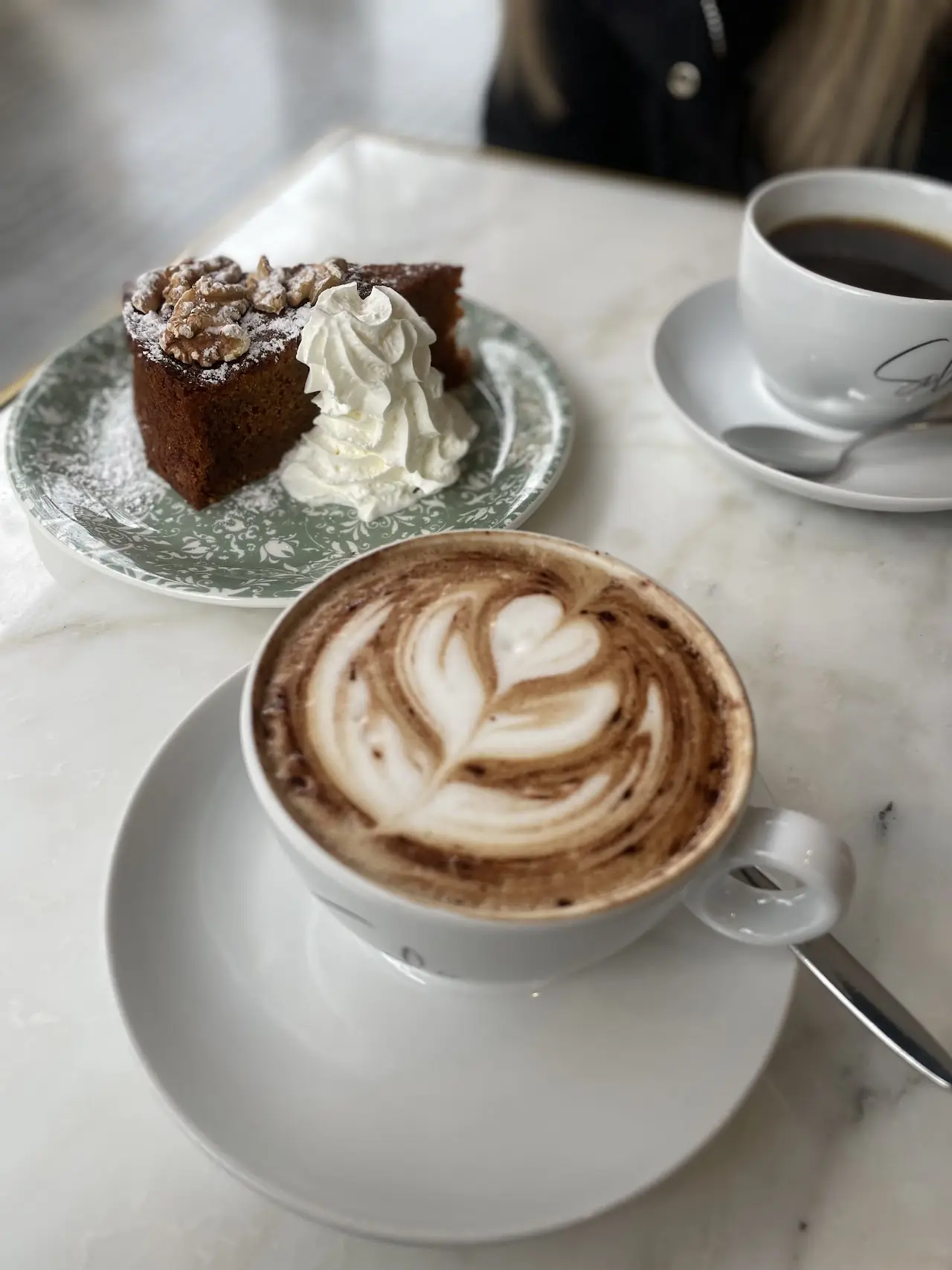 A slice of chocolate cake with whipped cream next to a cappuccino with latte art.