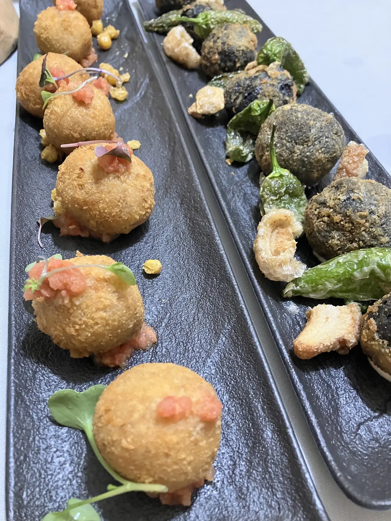 Croquettes and blistered green peppers on a long slate.