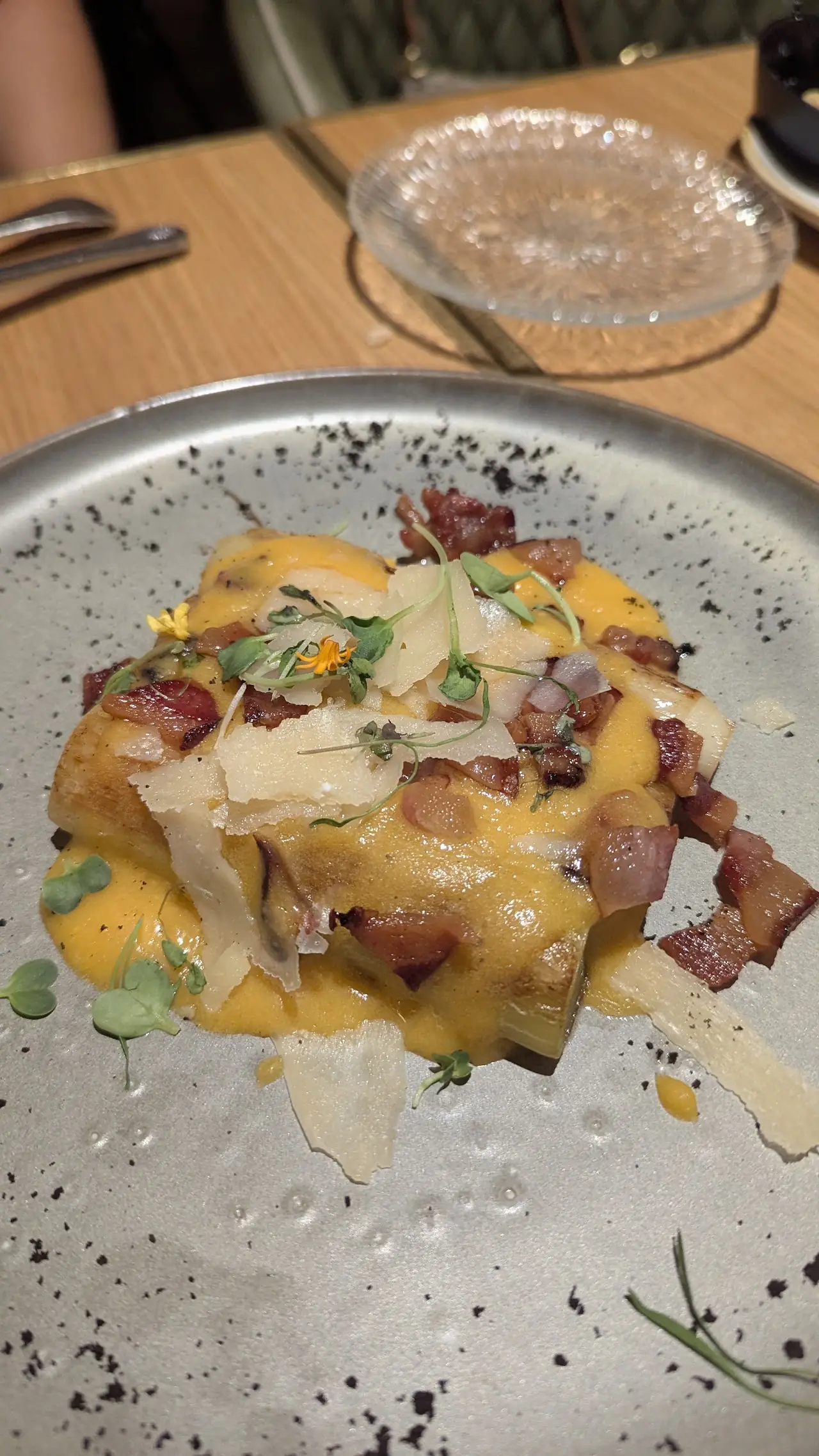 Pasta with bacon and shaved cheese on a speckled grey plate.