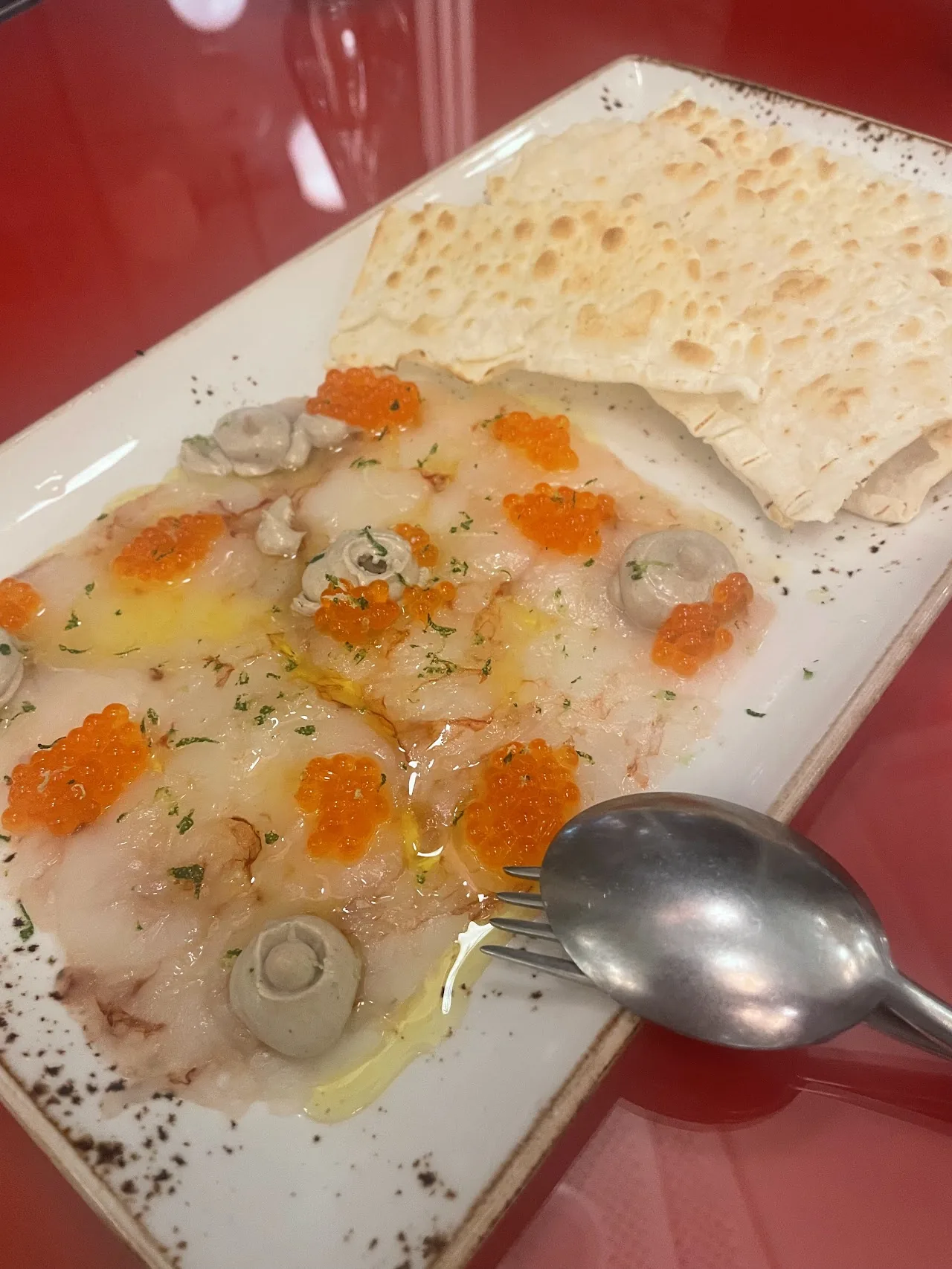 A flatbread topped with roe and herbs on a plate with a spoon